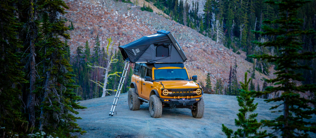 Yellow Bronco parked in the mountains with rooftop tent out